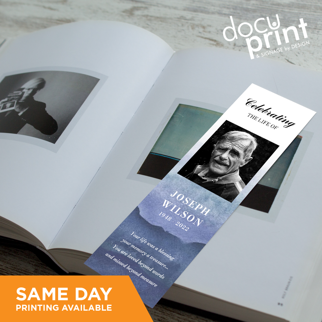 A bookmark with a black and white image of a person and text, placed on an open book, custom designed and printed by Docuprint in Fremantle, Perth, Australia