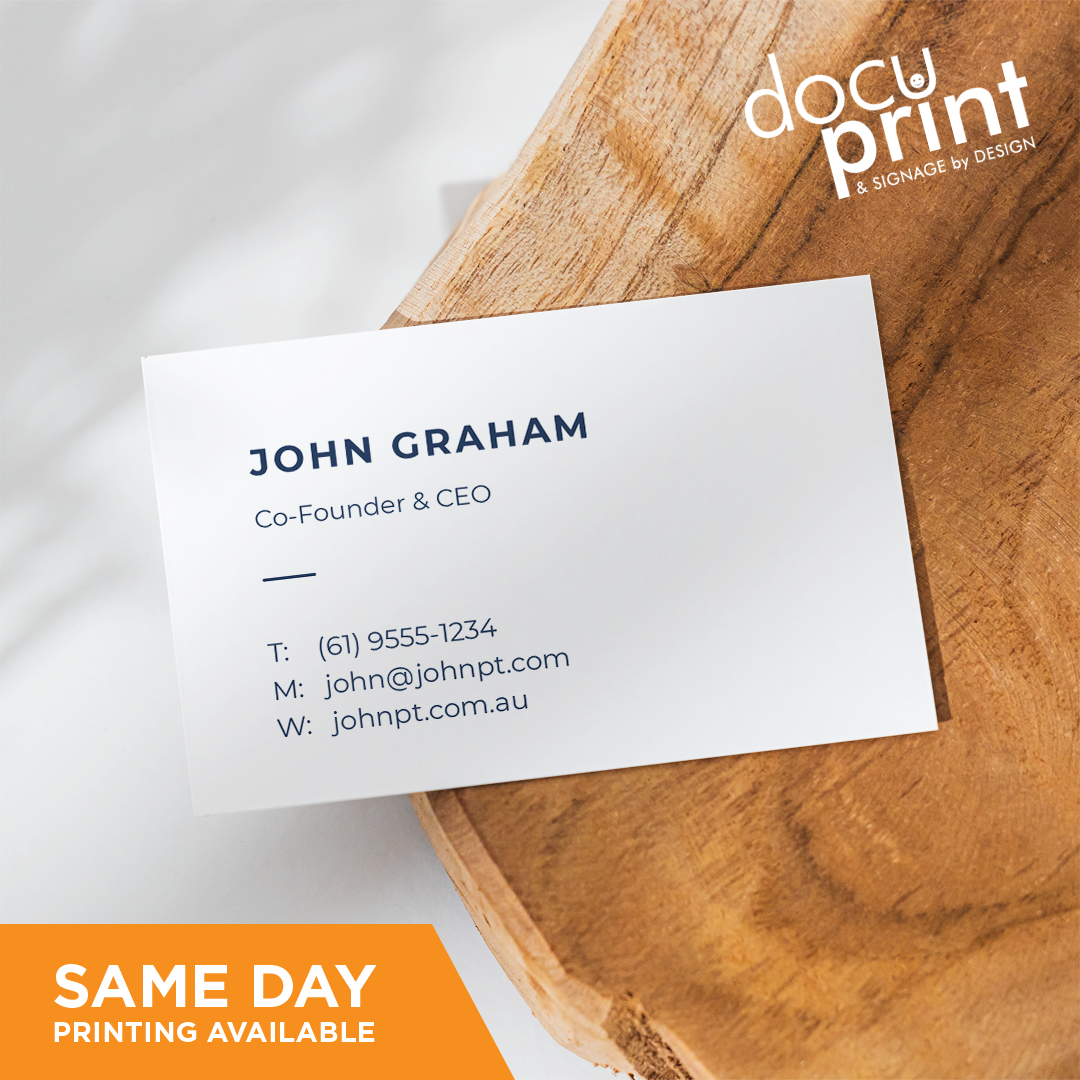 A white business card with black text and a company logo, placed on a wooden surface. The text includes a name, job title, company name, address, phone number, and email, custom designed and printed by Docuprint in Fremantle, Perth, Australia.