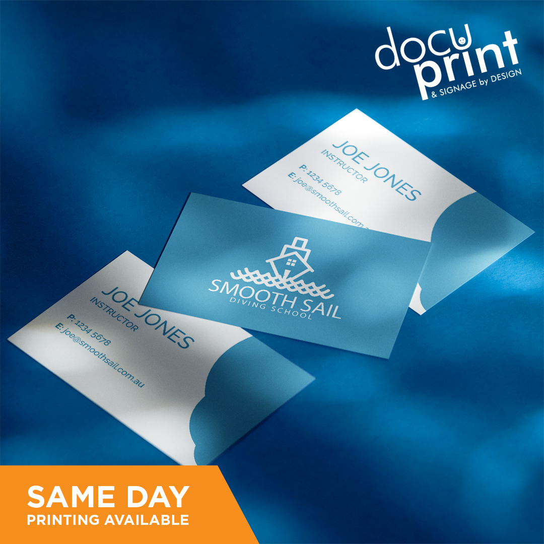 A set of business cards with a blue background, featuring text and a company logo, custom designed and printed by Docuprint in Fremantle, Perth, Australia. The business cards are placed on a fabric surface with a shadow falling over them.