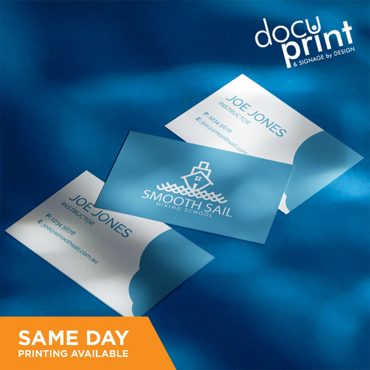 A set of business cards with a blue background, featuring text and a company logo, custom designed and printed by Docuprint in Fremantle, Perth, Australia. The business cards are placed on a fabric surface with a shadow falling over them.
