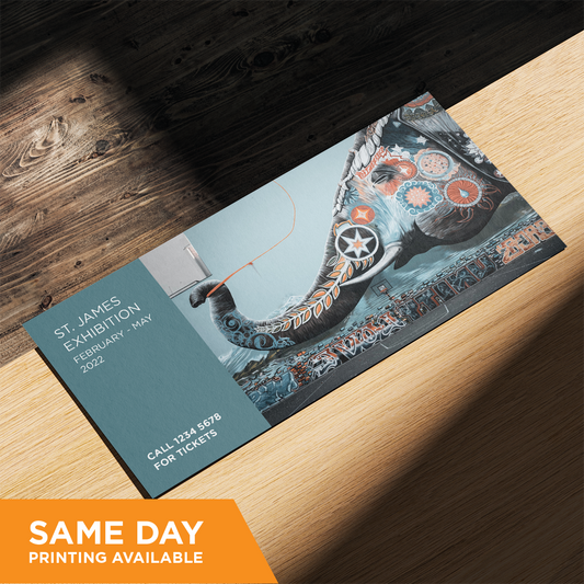 A double-sided DL card with a colorful illustration on the front, lying on a wooden surface. The illustration features a stylized, artistic depiction of an elephant, custom designed and printed by Docuprint in Fremantle, Perth, Australia