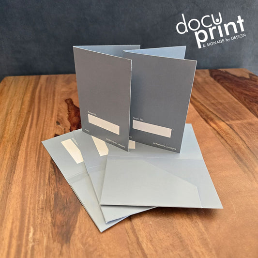 grey hotel key card holders spread out on a wooden table. Custom made, designed and printed by Docuprint Fremantle in WA.