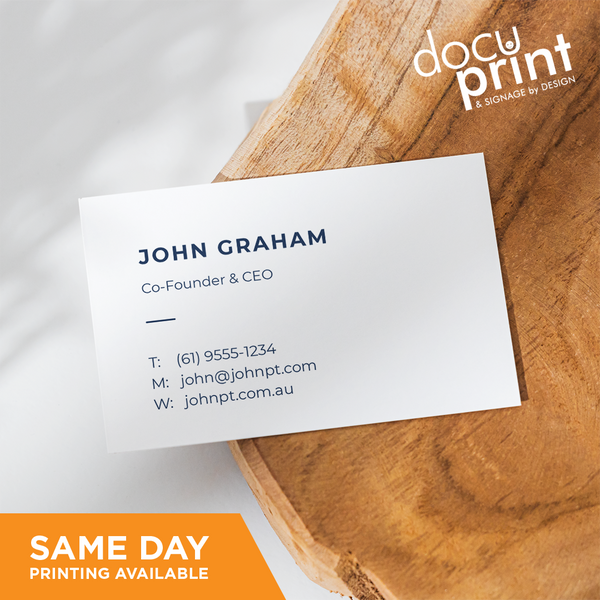 A white business card with black text and a company logo, placed on a wooden surface. The text includes a name, job title, company name, address, phone number, and email, custom designed and printed by Docuprint in Fremantle, Perth, Australia. 