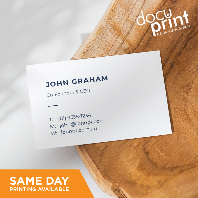 A white business card with black text and a company logo, placed on a wooden surface. The text includes a name, job title, company name, address, phone number, and email, custom designed and printed by Docuprint in Fremantle, Perth, Australia. 