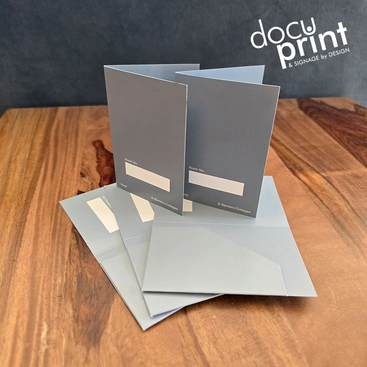 grey hotel key card holders spread out on a wooden table. Custom made, designed and printed by Docuprint Fremantle in WA. 